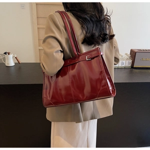 Detail showing the burgundy glossy tote bag carried over the shoulder by a model