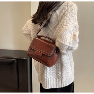 Detail of vintage reddish-brown crossbody bag with white stitching and woven strap
