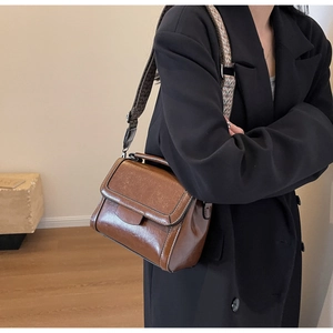 Detail of vintage brown leather handbag featuring a wide ethnic woven strap in an indoor setting