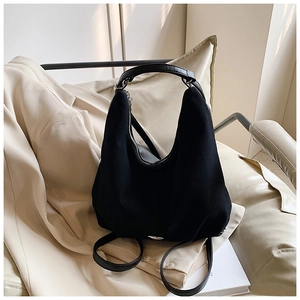 Detail of minimalist black hobo tote bag placed on a cream blazer for workplace style