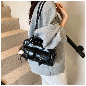 Detail of glossy black Boston bag with functional buckle pockets and baseball tassel charm