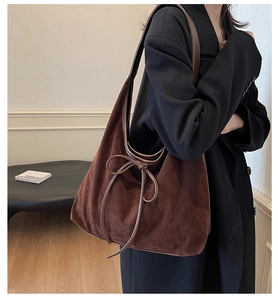 Detail view of large dark brown suede tote bag with a decorative leather bow on shoulder