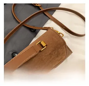Close-up of golden metal buckle and brown leather-suede stitching on the crossbody bag