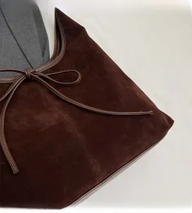 Detailed view of dark brown suede hobo bag featuring a leather bow knot and piping detail