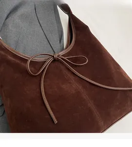 Detail of dark brown suede shoulder bag featuring slim leather ribbon bow decoration