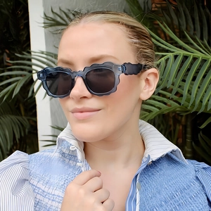 Modern wavy cloud edge sunglasses with blue-grey frame on a model in a tropical setting