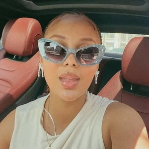 Blue glitter cat-eye sunglasses with grey gradient lenses worn by model in a car