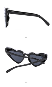 Detail view of heart-shaped sunglasses featuring white pearls on the black frame