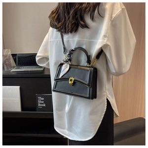 Detail of black square bag with golden horseshoe clasp and printed silk scarf on handle