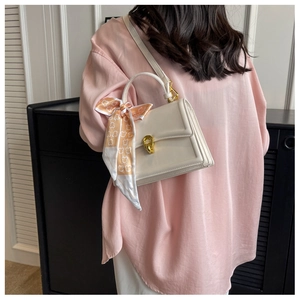 Detail of a beige square handbag with gold metal clasp and floral scarf on the handle