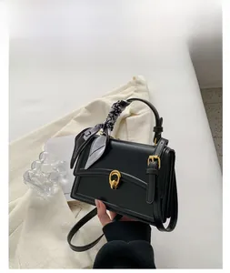 Detail of black square handbag with a decorative silk scarf and gold twist lock