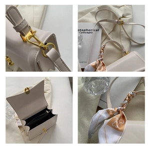 Detail view of cream square handbag with gold hardware and silk scarf on handle