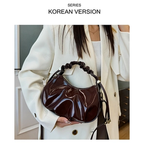 Detail of glossy pleated dark brown dumpling bag with crossbody strap on a white suit