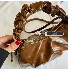 Close-up of smooth gold zipper and pleated texture on brown leather dumpling bag