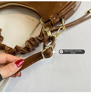 Detail of adjustable shoulder strap and gold buckle on brown oil wax leather cloud bag