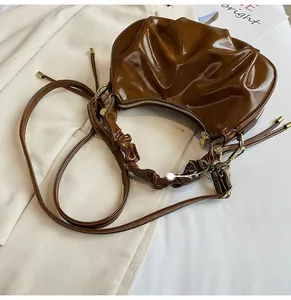 Detail of adjustable pleated shoulder strap on a brown glossy croissant hobo handbag