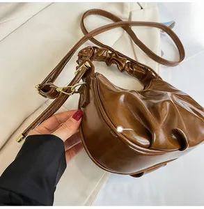 Detail of a brown ruched handbag featuring a crescent shape and gold metal hardware