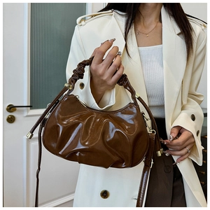 Detail of a brown pleated cloud bag featuring shiny oil-wax leather and gold buckles