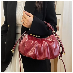 Detail of burgundy ruched dumpling bag with glossy finish and gold metal hardware studs