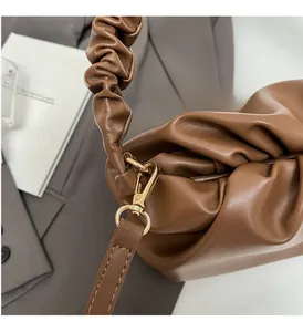 Close-up of golden metal hooks and brown pleated leather texture on a cloud bag
