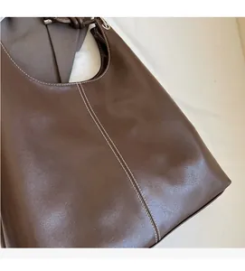 Detail of brown leather tote showing white stitching and soft textured fabric surface