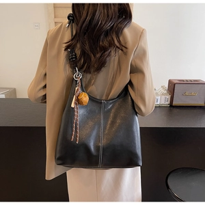 Detail of a large black leather tote bag with white stitching shown on a person shoulder