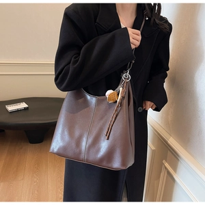 Detail of dark brown leather tote bag with white stitching and baseball glove charm