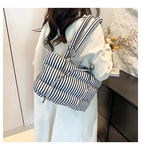 Détail d'un sac cabas rembourré à rayures noires et blanches porté sur un manteau beige