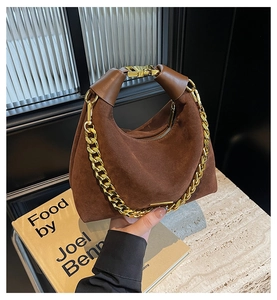 Detail of a brown suede hobo bag featuring a decorative gold chain and metallic logo plate