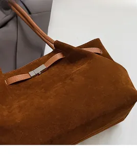 Detail of dark brown matte suede bucket bag with silver metal buckle and leather handle