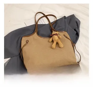 Detail of khaki tote bag with brown leather straps and teddy bear charm on a blazer