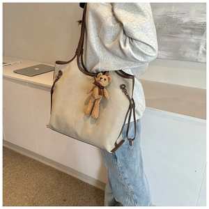 Close-up of a large beige canvas tote bag with brown leather trim and a plush bear charm