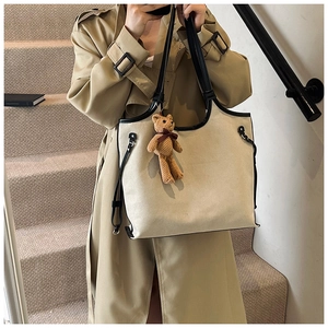 Close-up of a large beige canvas tote bag with black trim and a brown teddy bear pendant