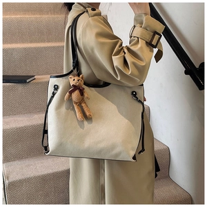 Detail of a large cream canvas tote bag with black leather straps and a knit bear charm