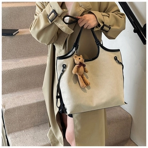 Detailed side view of off-white canvas tote bag with black leather trim and bear pendant