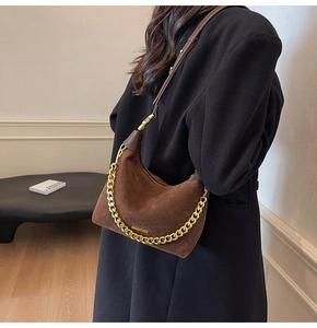 Detailed macro of brown suede crescent bag featuring gold chain and metallic hardware