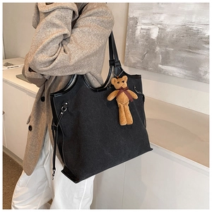 Detail of a large black canvas tote bag with leather trim and a cute bear charm pendant