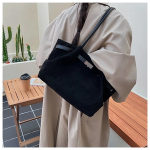 Detail view of large black matte suede tote bag with silver metal buckle on a wood table
