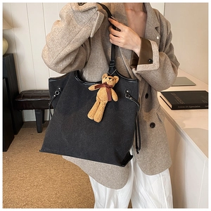 Large black canvas tote bag shown with cute teddy bear charm in a stylish office setting