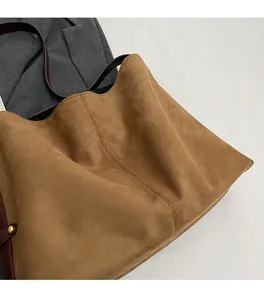Detail of soft brown suede tote bag featuring metallic rivets and reinforced stitching