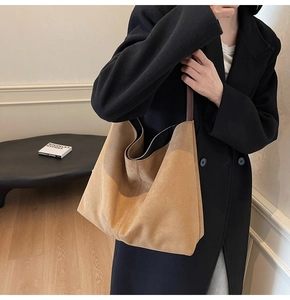 Detail of a large khaki suede tote bag carried by a model wearing a long black coat