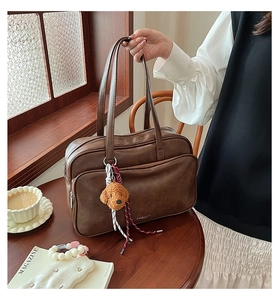 Detail of a brown leather Boston bag with a cute dog plush charm on a wooden table