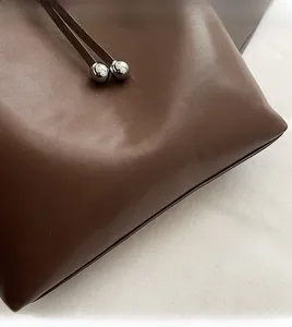 Dettaglio della borsa a secchiello in pelle marrone scuro con perline metalliche e logo