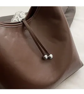 Dettaglio borsa a secchiello in pelle marrone con coulisse e perla in metallo