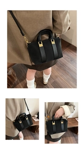 Detail of black tote bag with gold hardware worn by model in brown blazer