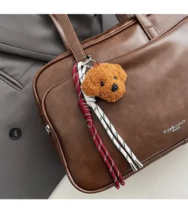 Detail of a brown Boston bag with a teddy bear charm and woven tassels on grey fabric