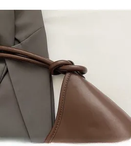 Dettaglio di una borsa a secchiello in pelle marrone con tracolla a nodo e cuciture