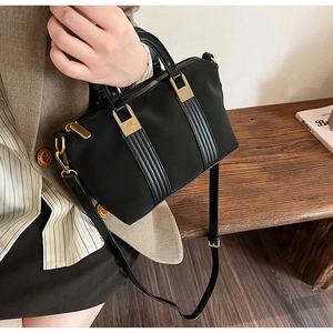 Detail of black nylon and leather Boston bag held by model against a minimalist background