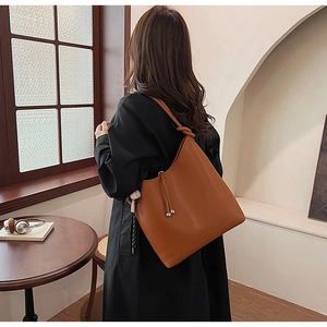 Dettaglio di una borsa tote in pelle marrone con nodo raffinato e trama opaca sulla tracolla