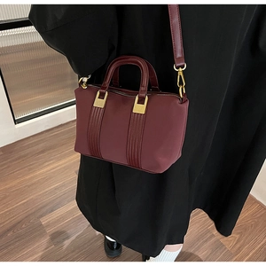 Detail of burgundy leather Boston bag with gold metal hardware and adjustable shoulder strap